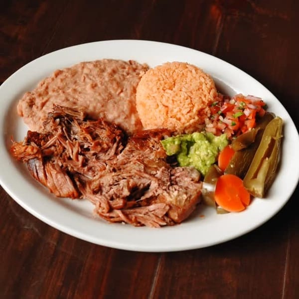 Delicious Mexican plate with shredded meat, refried beans, rice, guacamole, salsa, and pickled vegetables.