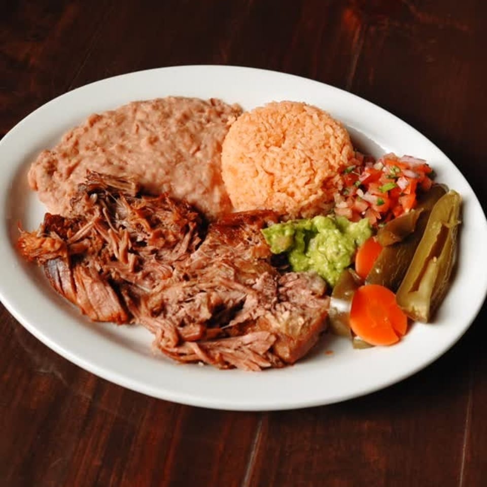 Delicious Mexican plate with shredded meat, refried beans, rice, guacamole, salsa, and pickled vegetables.