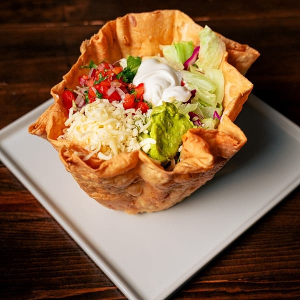 Taco salad in a crispy tortilla bowl with lettuce, cheese, pico de gallo, sour cream, and guacamole.