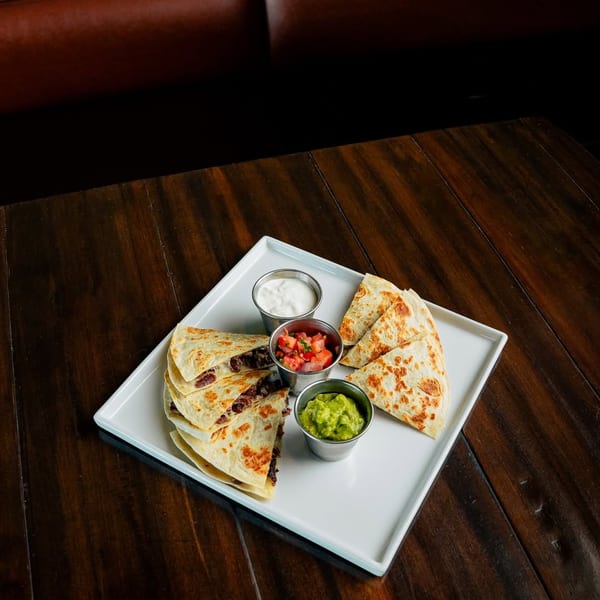Black bean quesadillas with guacamole, pico de gallo, and sour cream on a wooden table.