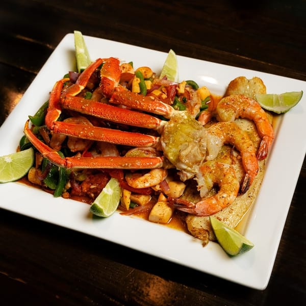 Seafood platter with crab legs, shrimp, and vegetables, garnished with lime wedges.