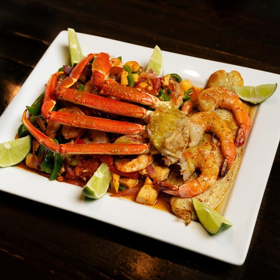 Seafood platter with crab legs, shrimp, and vegetables, garnished with lime wedges.