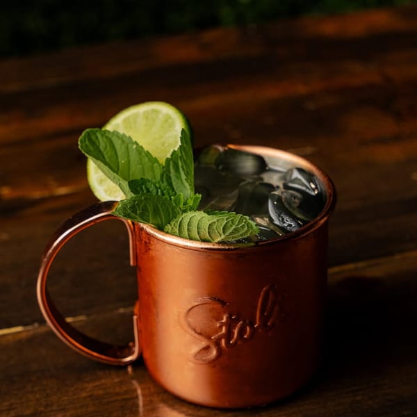 Stol copper mug with a refreshing drink, ice, lime, and mint on a wooden table.