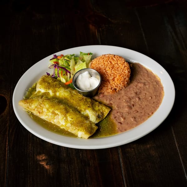 Two green enchiladas with rice, refried beans, a side salad, and sour cream on a white plate.